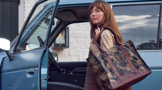 A woman holding a camouflage-patterned tote bag stands next to an open car door, looking towards the camera.