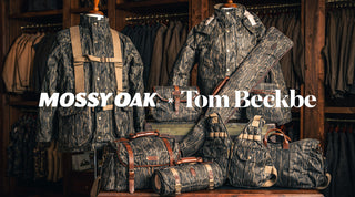 A collection of Mossy Oak and Tom Beckbe camouflage jackets, bags, and cases displayed in a wood-paneled store.