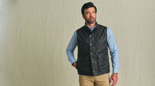 An olive green utility vest with snap buttons and multiple front pockets, laid flat on a brown surface.