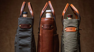 Three wine tote bags, each containing a bottle and featuring leather handles and personalized leather tags with initials: RKM, DTB, and THB.