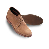 A pair of Tom Beckbe Alden #1494 Unlined Chukka Boots in light brown suede, one upright, one showing the sole.