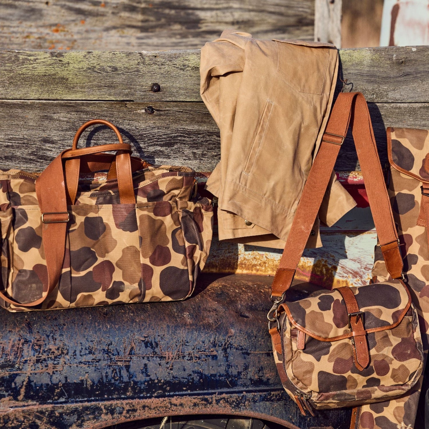 Classic Camo Blind Bag by Tom Beckbe and khaki pants hang on a wooden fence against a rusty backdrop.