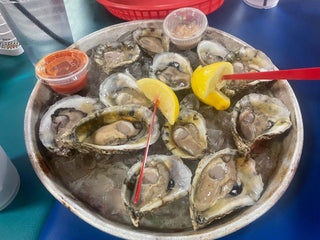A round tray of oysters on ice with lemon wedges and small containers of sauce.