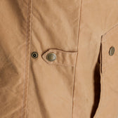 Close-up of the Tom Beckbe Kinsman Vest, a tan waxed canvas vest with metal snaps and detailed pocket stitching.