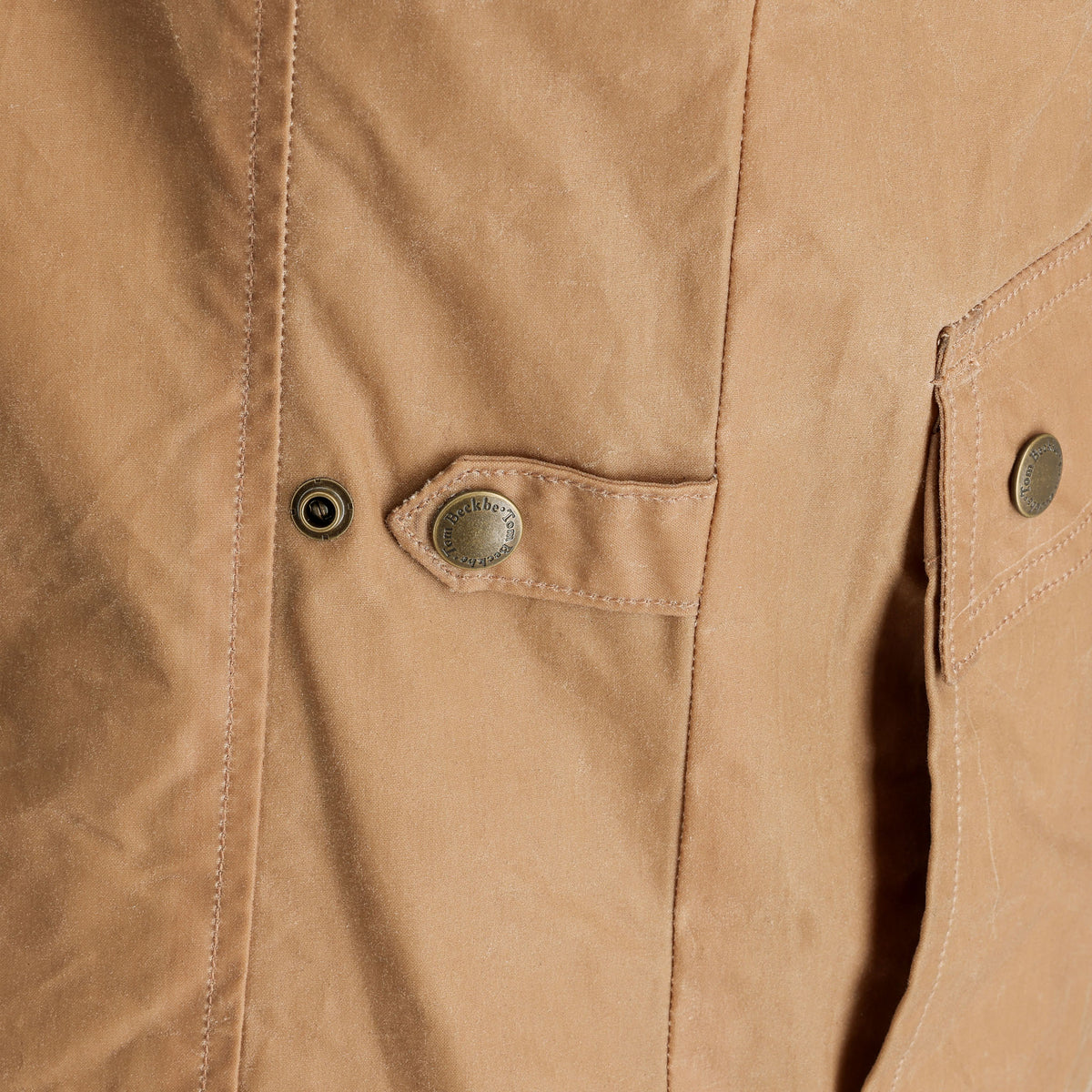 Close-up of the Tom Beckbe Kinsman Vest, a tan waxed canvas vest with metal snaps and detailed pocket stitching.