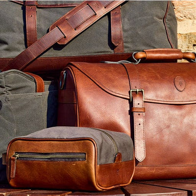 Brown leather bags and a gray canvas bag displayed on a flat surface with a yellow wall background.