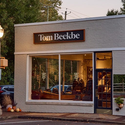 Storefront of Tom Beckbe with large windows, white brick exterior, and pumpkins outside. Trees and cars are in the background.
