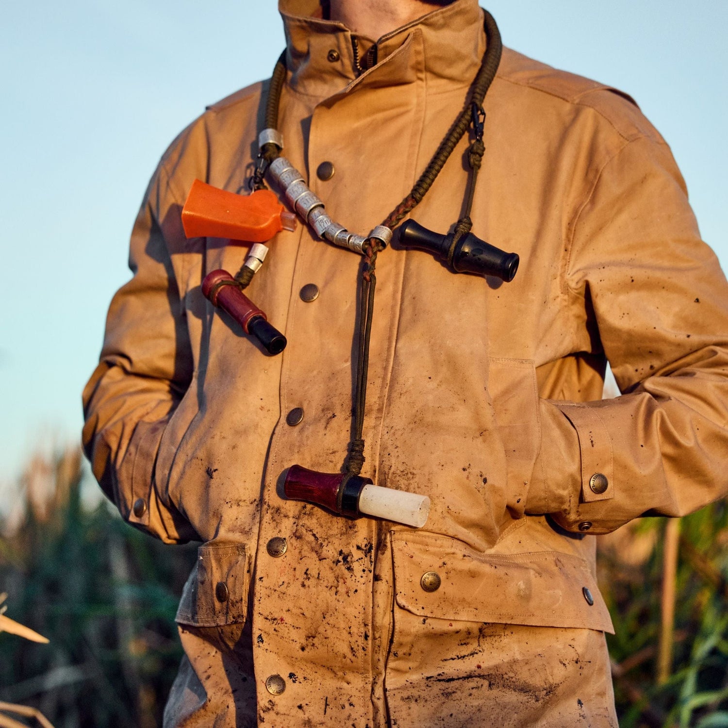 Wearing a Tom Beckbe Tensaw Jacket, a person stands outside with hands in pockets, duck calls on a lanyard.