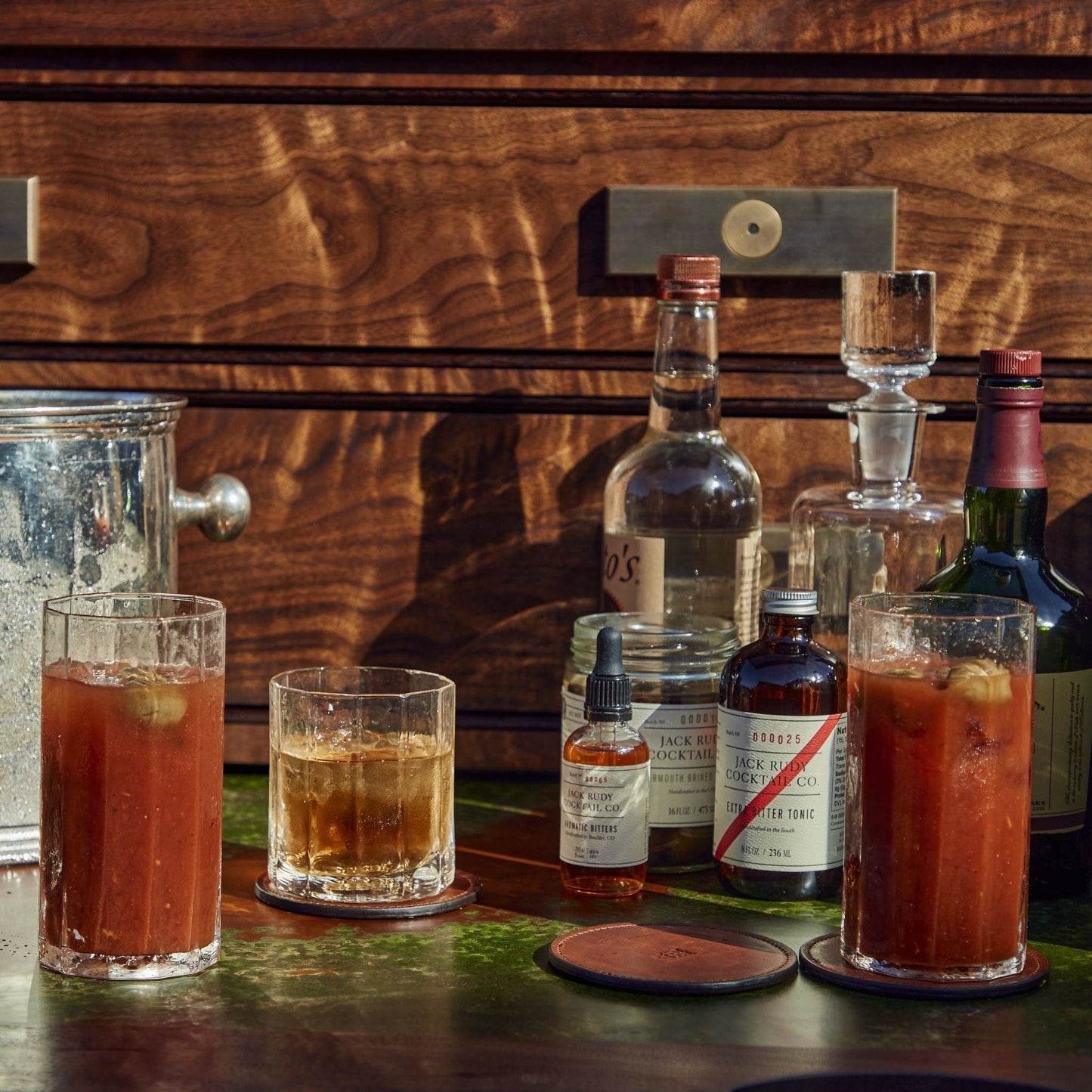 Terrane No. 12 Glasses by Tom Beckbe hold mixed drinks on a wooden table with ice and cocktail ingredients nearby.