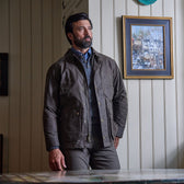 A man wears the Tom Beckbe Albemarle Henley Sweater, standing indoors by wood paneling and a framed painting.