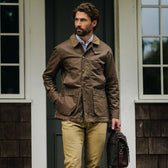 Man wearing a Tom Beckbe Baldwin Jacket and khaki pants stands outside, holding a brown bag in his left hand.