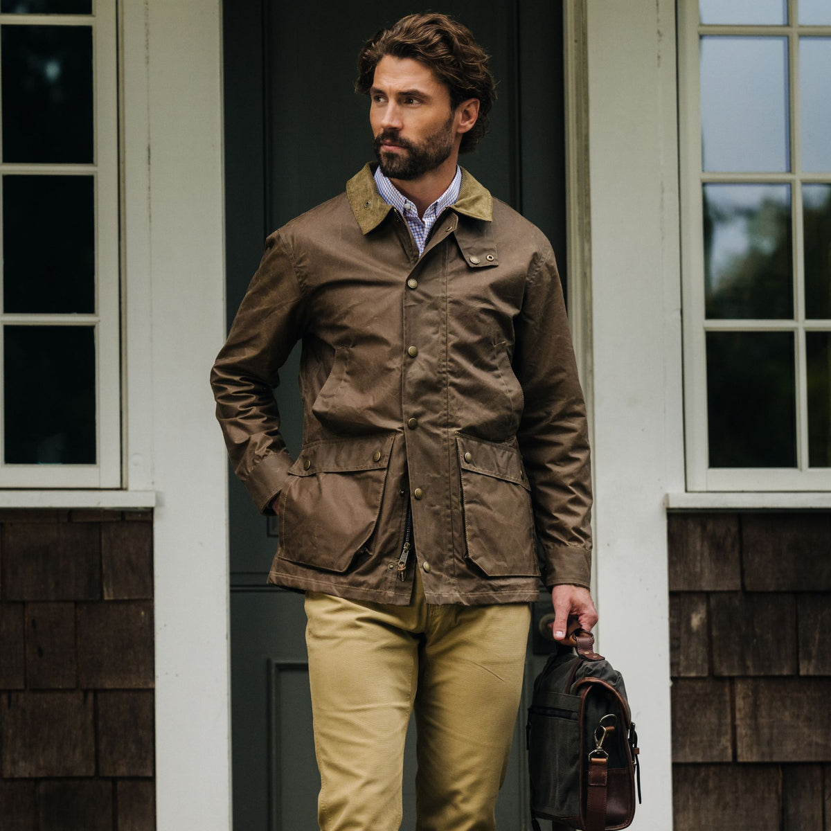 Man wearing a Tom Beckbe Baldwin Jacket and khaki pants stands outside, holding a brown bag in his left hand.