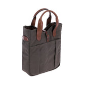Tom Beckbe Canvas Whiskey Tote in dark gray waxed canvas with brown leather handles and two front pockets, upright.