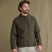 Man wears Tom Beckbe Burgess Quilted Jacket and light pants, standing against a plain tan background.