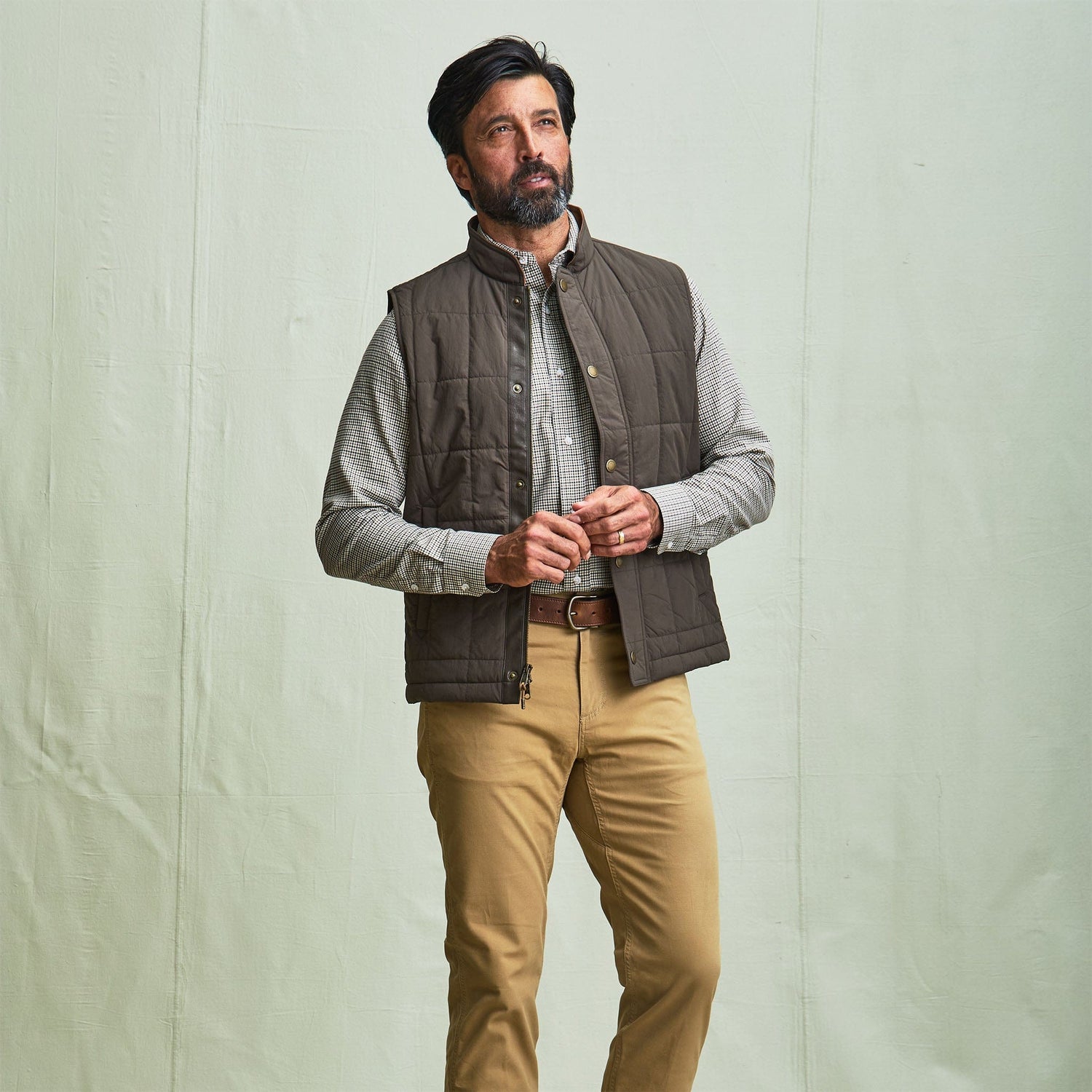 Man wearing the Tom Beckbe Burgess Quilted Vest, plaid shirt, and khaki pants against a plain light background.