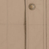 Close-up of the Tom Beckbe Burgess Quilted Vest in beige featuring detailed stitching and signature button.