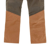 A close-up of Tom Beckbe's Burwell Brush Pant features brown fabric below the knees and dark gray above with a diagonal seam.
