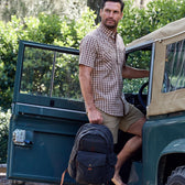 A man with a Tom Beckbe Canvas Backpack exits an off-road vehicle, surrounded by lush greenery.
