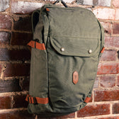 Tom Beckbe Canvas Daypack with leather accents and adjustable straps hangs on a brick wall.