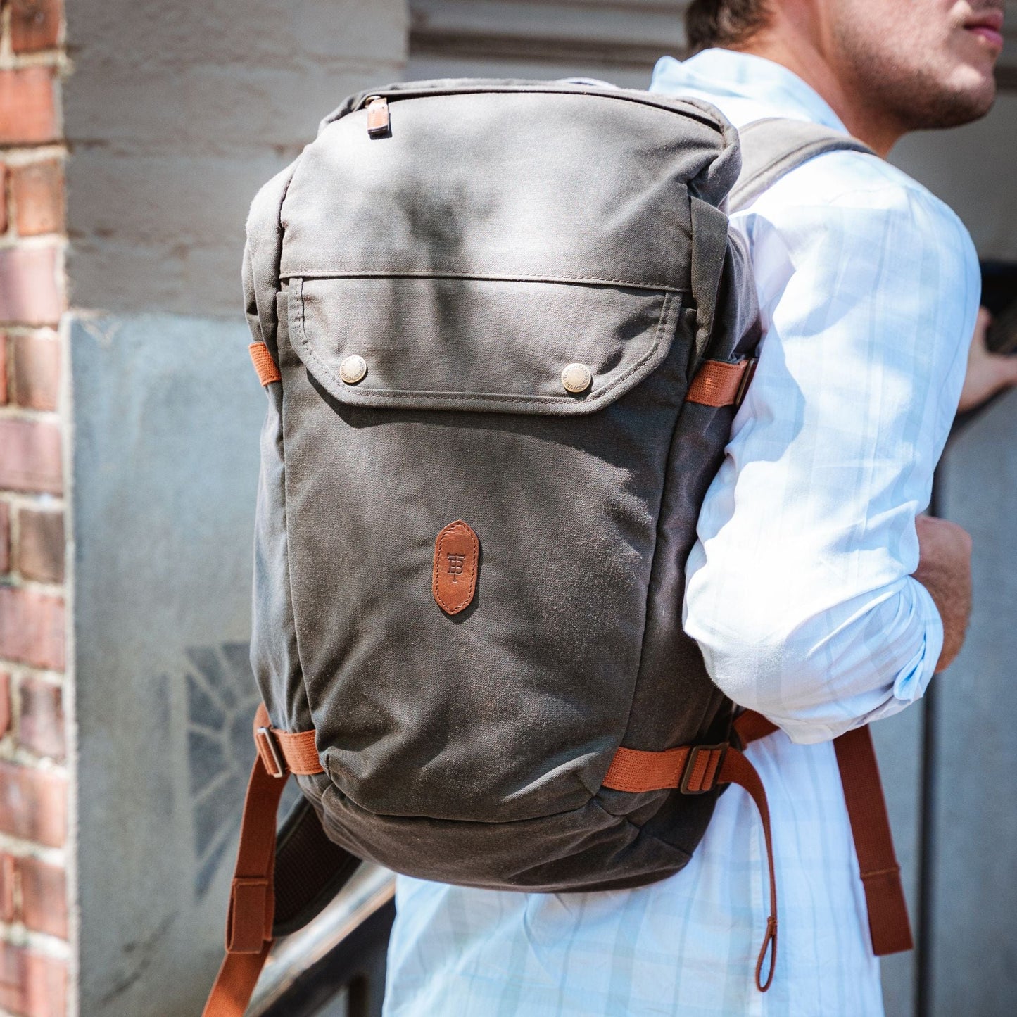 Person with a Tom Beckbe Canvas Daypack having adjustable straps, standing by a brick wall.