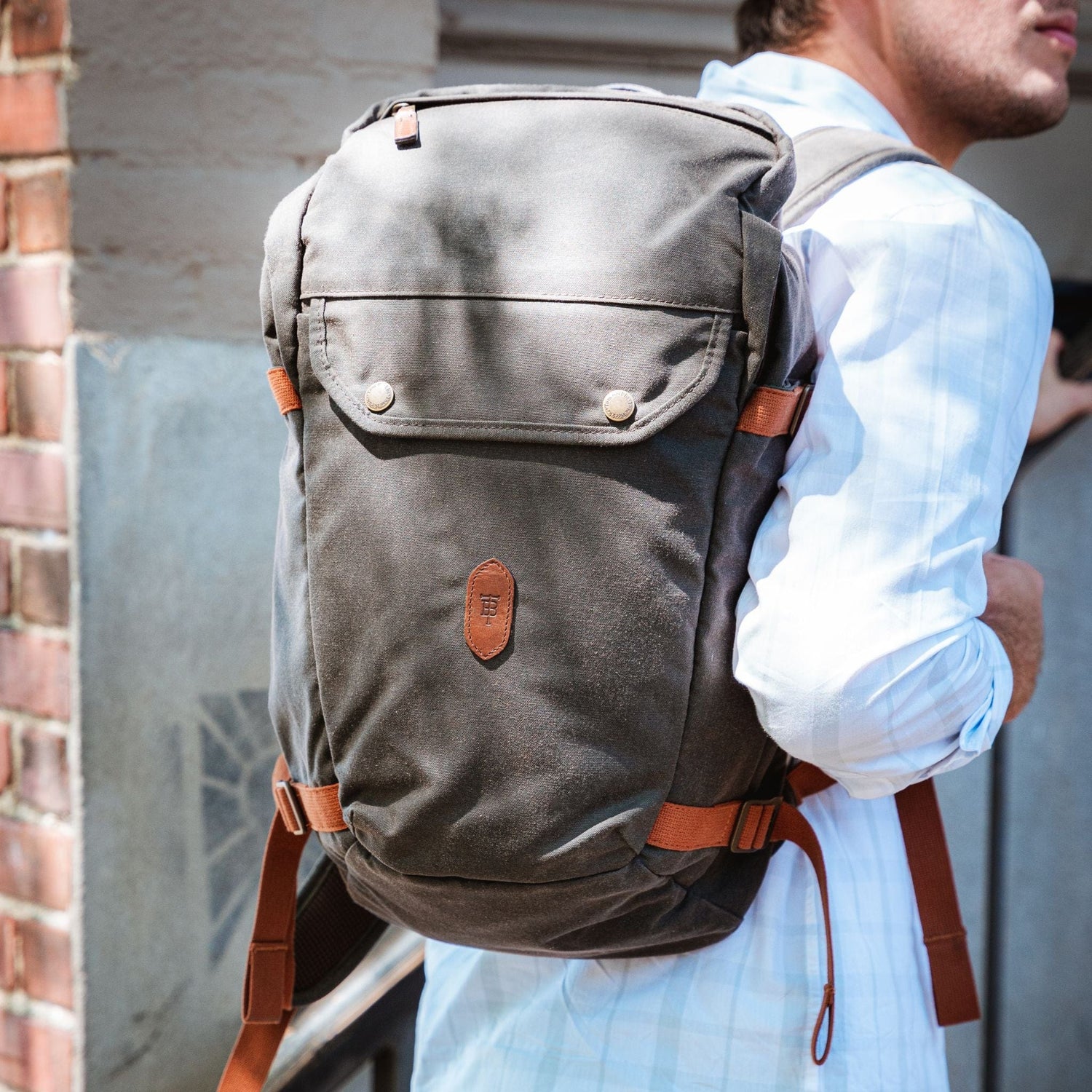 Person with a Tom Beckbe Canvas Daypack having adjustable straps, standing by a brick wall.