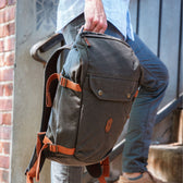 A person with a Tom Beckbe Canvas Daypack, featuring adjustable shoulder straps, walks up steps beside a brick wall.