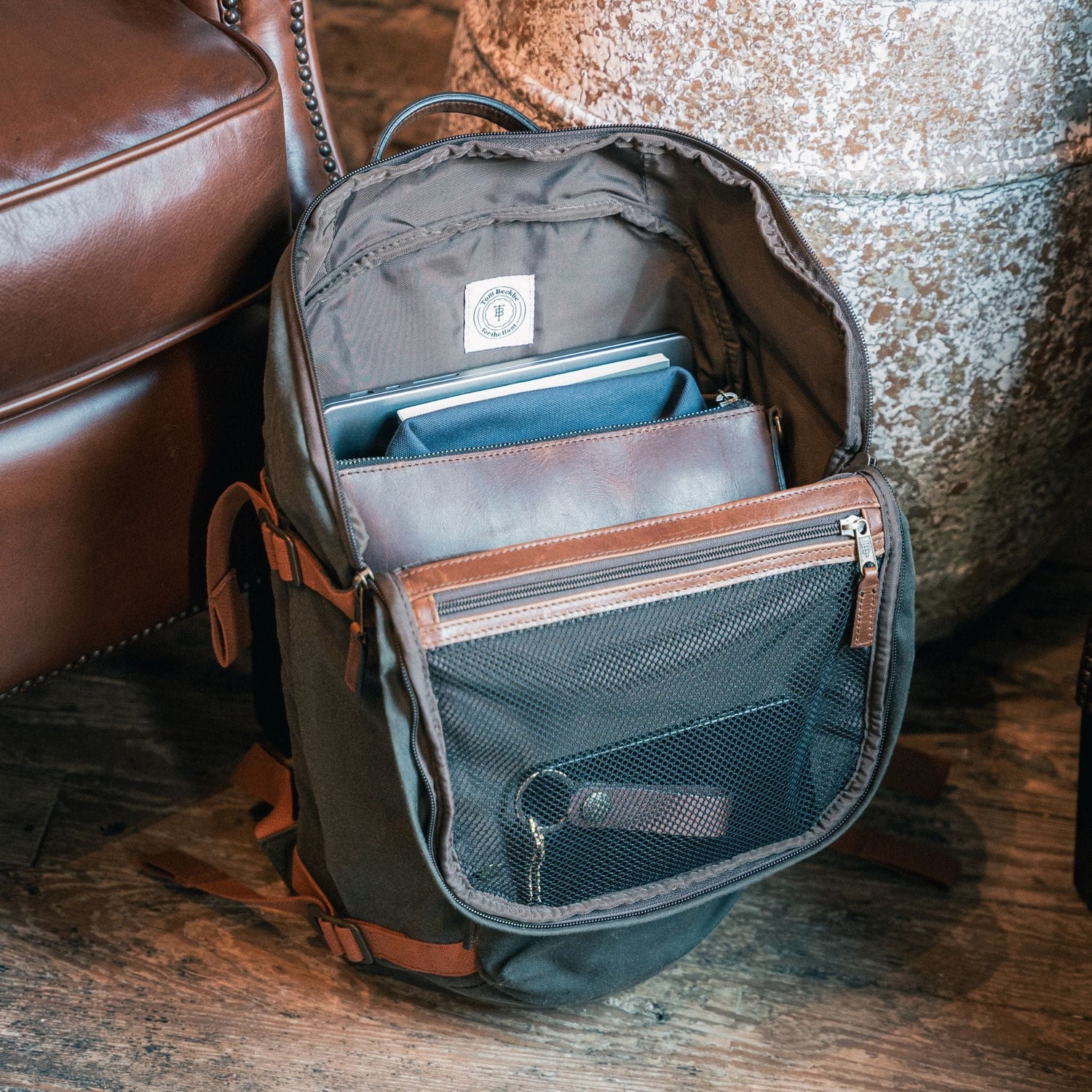 Tom Beckbe Canvas Daypack with adjustable straps holds a tablet, laptop, and leather folder on the floor.