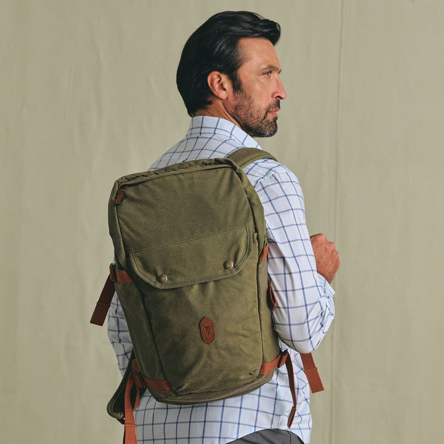 A man in a checkered shirt carries the Tom Beckbe Canvas Daypack with padded laptop sleeve, facing sideways.