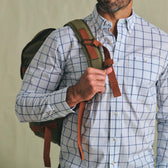 A man in a blue checked shirt carries his Tom Beckbe Canvas Daypack over one shoulder, holding the strap with one hand.