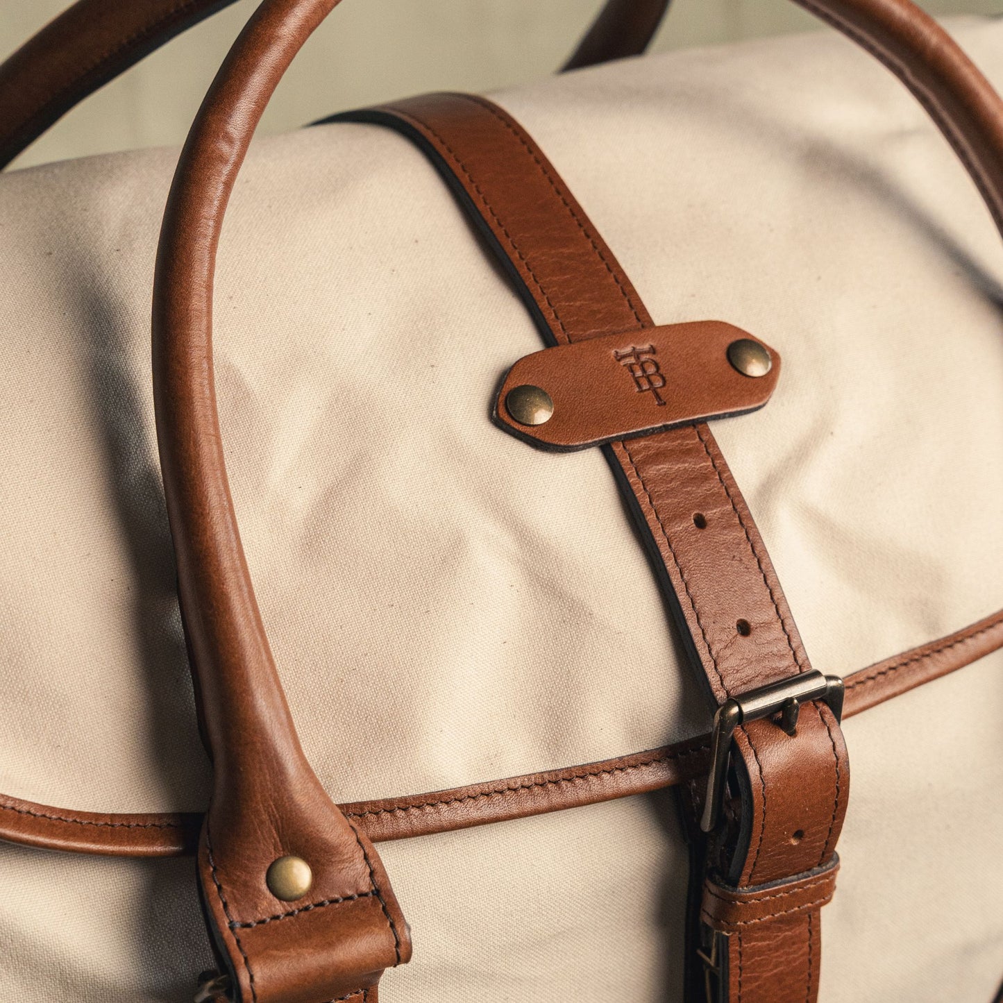 Close-up of the Perdido Canvas Weekender Duffel Bag by Tom Beckbe, featuring brown leather handles and embossed logo.