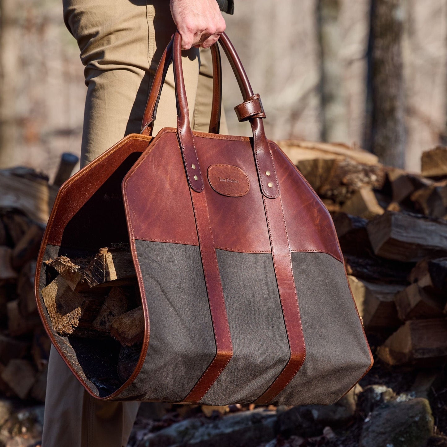 Carrying firewood in a Tom Beckbe Canvas Log Carrier, made of brown leather and black field canvas.