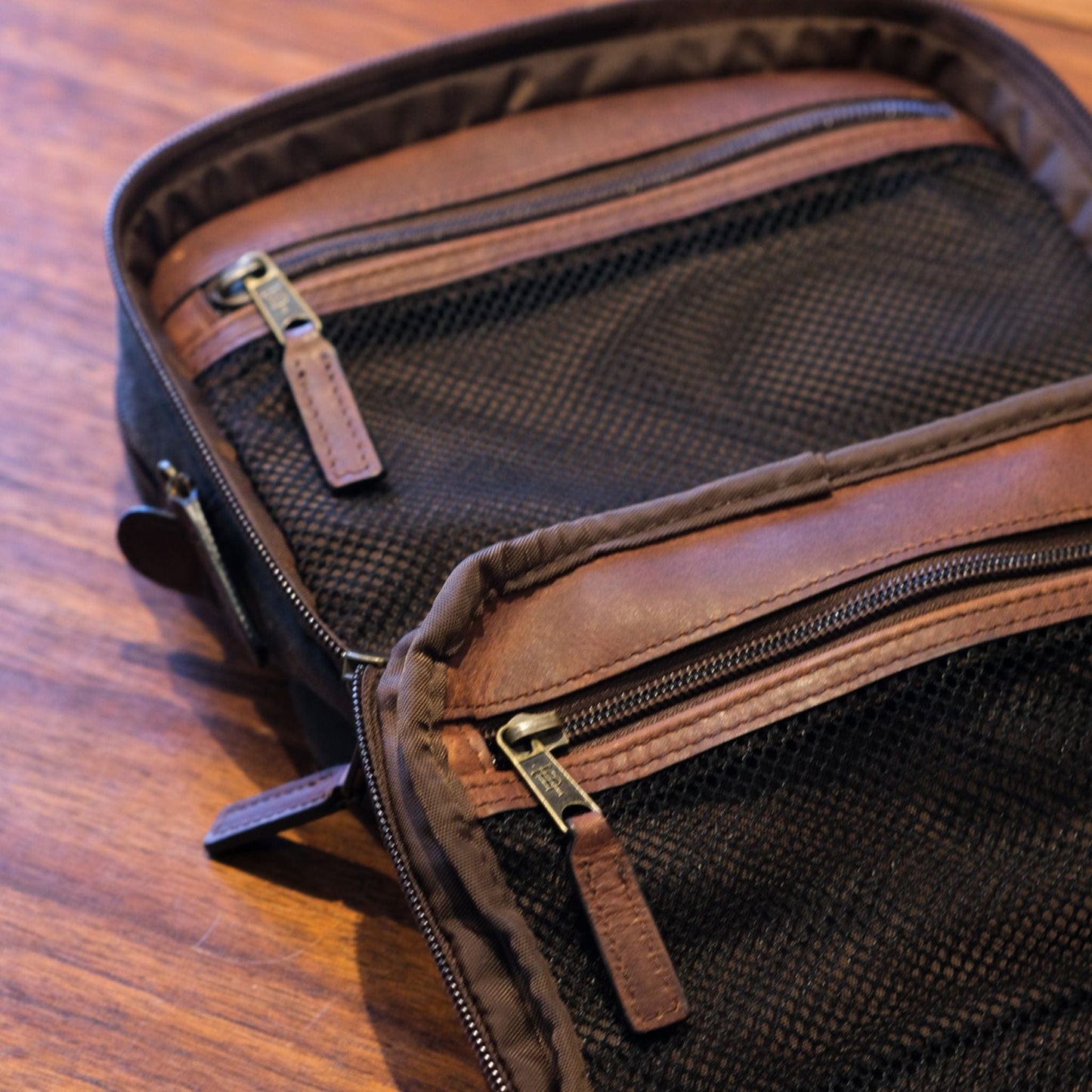 Tom Beckbes Canvas Hanging Toiletry Bag features mesh zippered compartments, resembling a sleek dopp kit on wood.