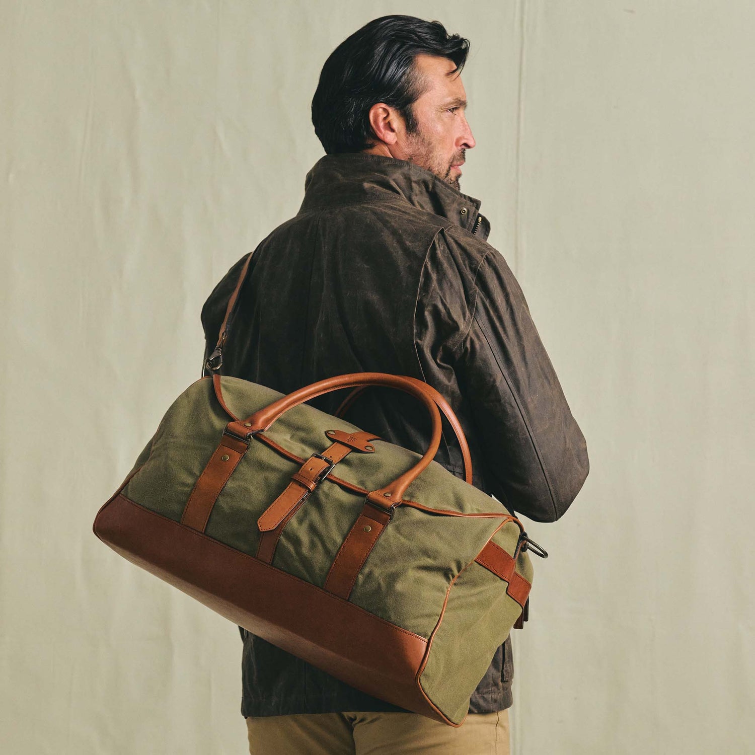 Man with a Tom Beckbe Canvas Weekender Duffel Bag over his shoulder, wearing a brown jacket, facing away.