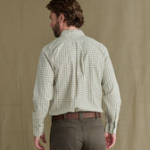 Man with brown hair wearing a light plaid shirt and dark pants, seen from behind, standing against a plain background.