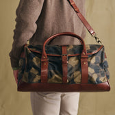 Person carrying a Tom Beckbe Classic Camo Weekender Duffel Bag, shown from the back with brown leather accents.