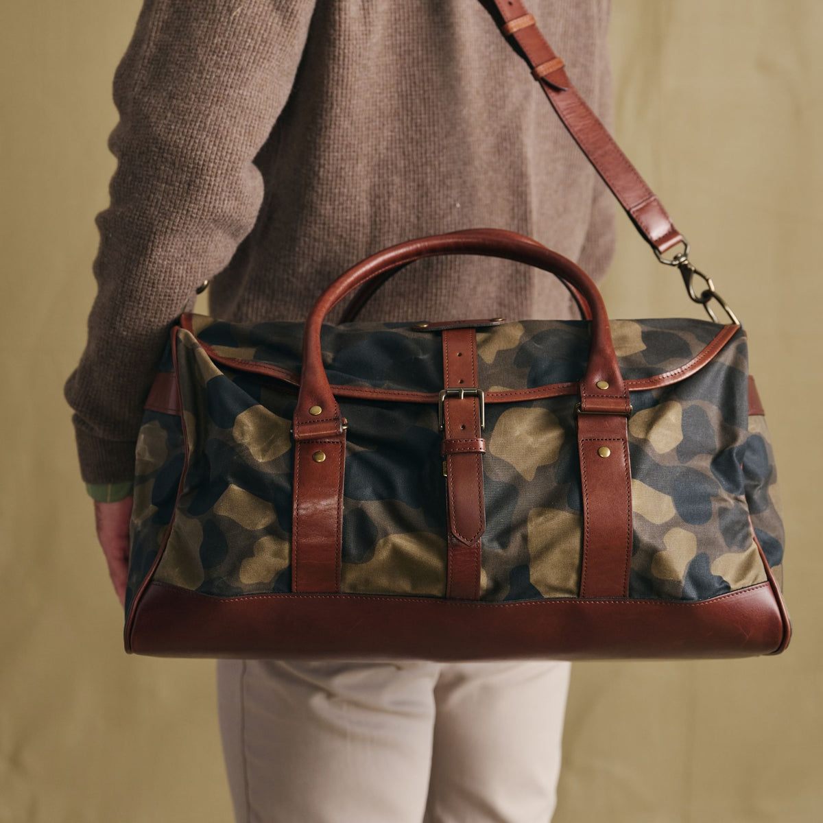 Person carrying a Tom Beckbe Classic Camo Weekender Duffel Bag, shown from the back with brown leather accents.