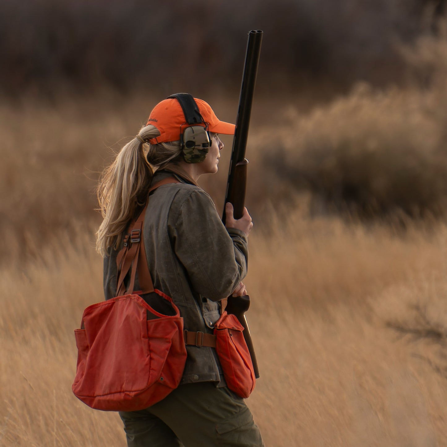 Person wearing a Tom Beckbe Cotton Twill Baseball Hat, ear protection, and holding a shotgun outdoors.