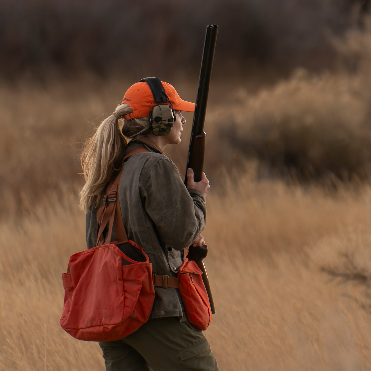 Person wearing a Tom Beckbe Cotton Twill Baseball Hat, ear protection, and holding a shotgun outdoors.