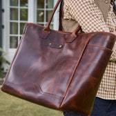 A person carries the Tom Beckbe Covington Leather Carryall Bag, wearing a checked shirt and tan vest.