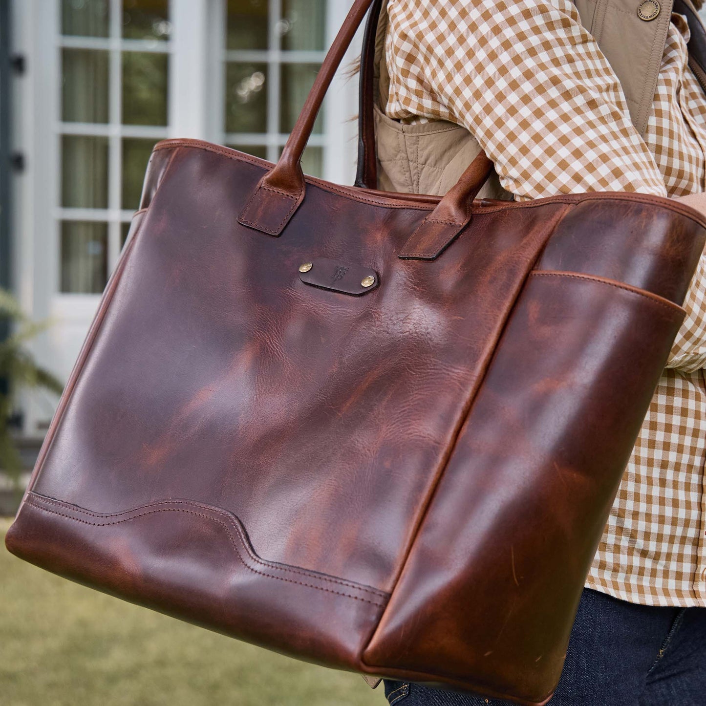 A person carries the Tom Beckbe Covington Leather Carryall Bag, wearing a checked shirt and tan vest.