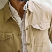 A man wears a Tom Beckbe Crawford Jacket in beige over a white plaid button-up shirt, shown from shoulders to chest.