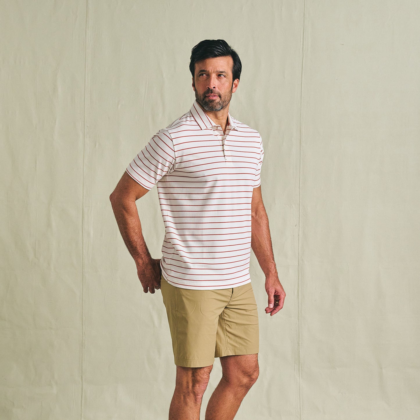 Man in Tom Beckbe Crenshaw Performance Short and striped polo stands against a plain background, looking to the side.