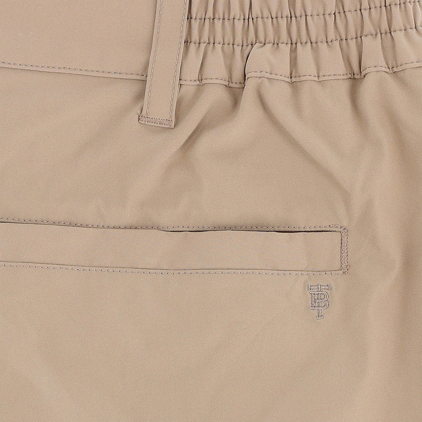 Close-up of Tom Beckbe Crenshaw Performance Short in beige, featuring elastic waistband, belt loop, welt pocket, and logo.