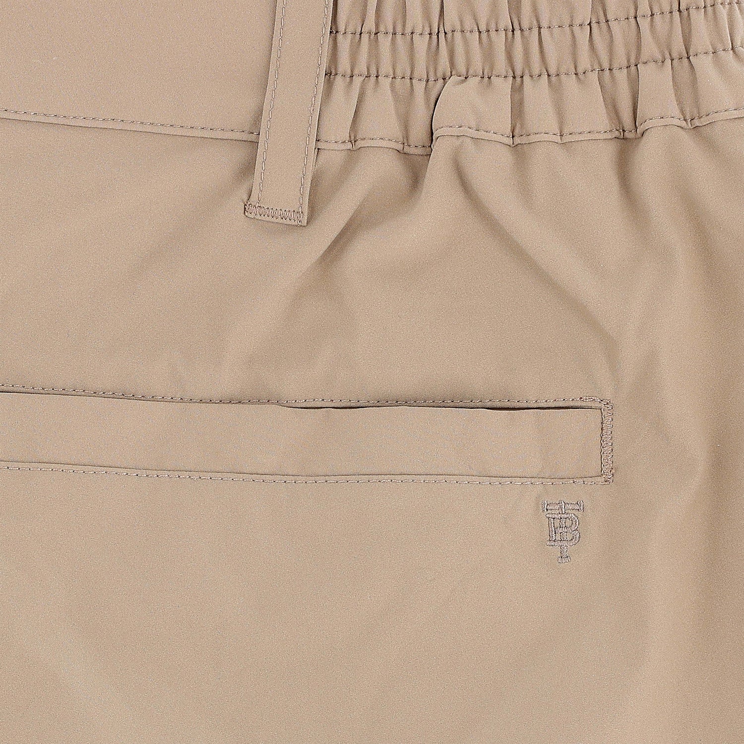Close-up of Tom Beckbe Crenshaw Performance Short in beige, featuring elastic waistband, belt loop, welt pocket, and logo.