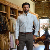 A man in a Tom Beckbe Culver Oxford Shirt and brown pants stands in a store with racks of jackets and shirts.