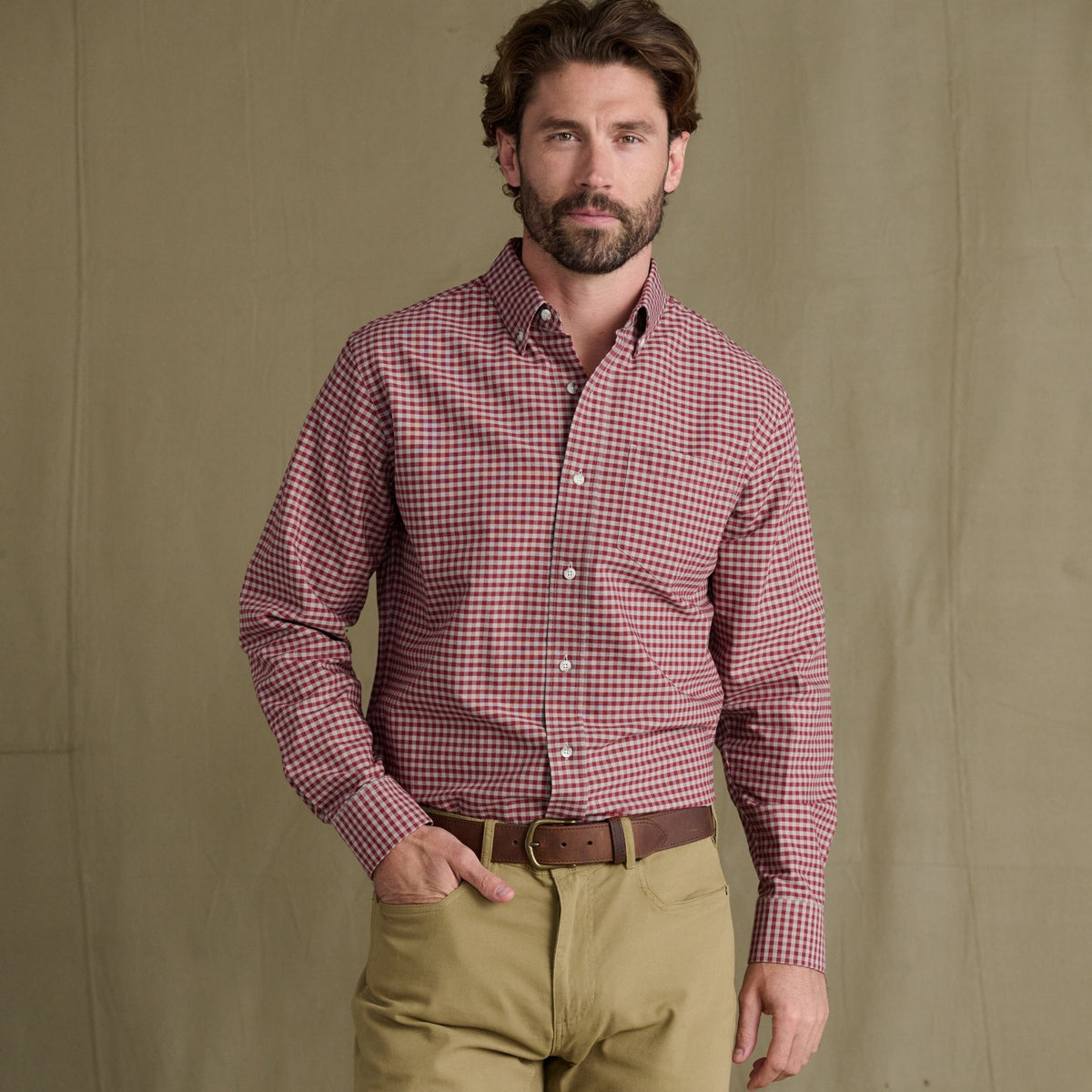 Man in Tom Beckbe Culver Oxford Shirt, red checkered cotton, and khaki pants stands before a plain beige backdrop.