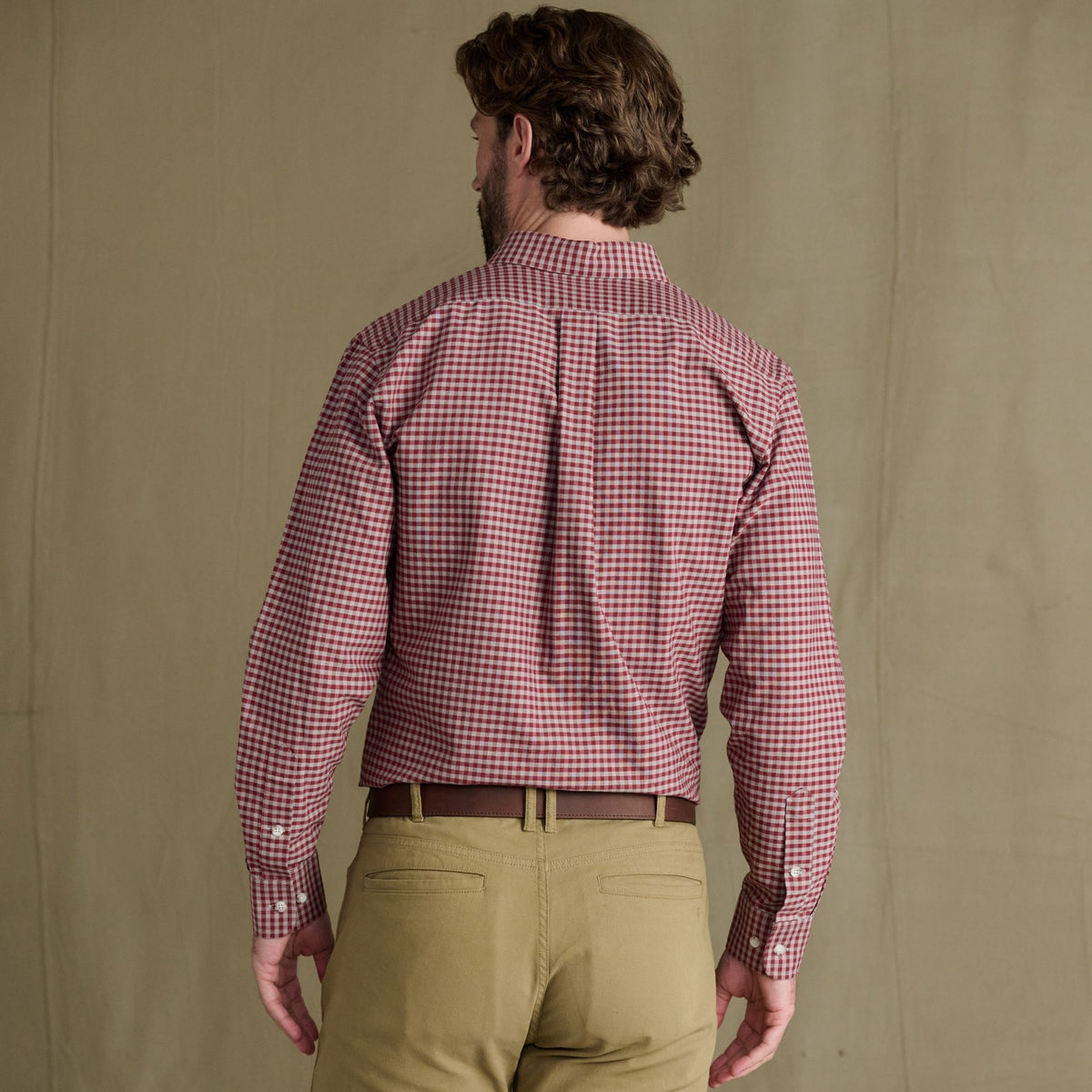 Man wears red check Culver Oxford Shirt by Tom Beckbe with tan pants, back to camera, against plain background.