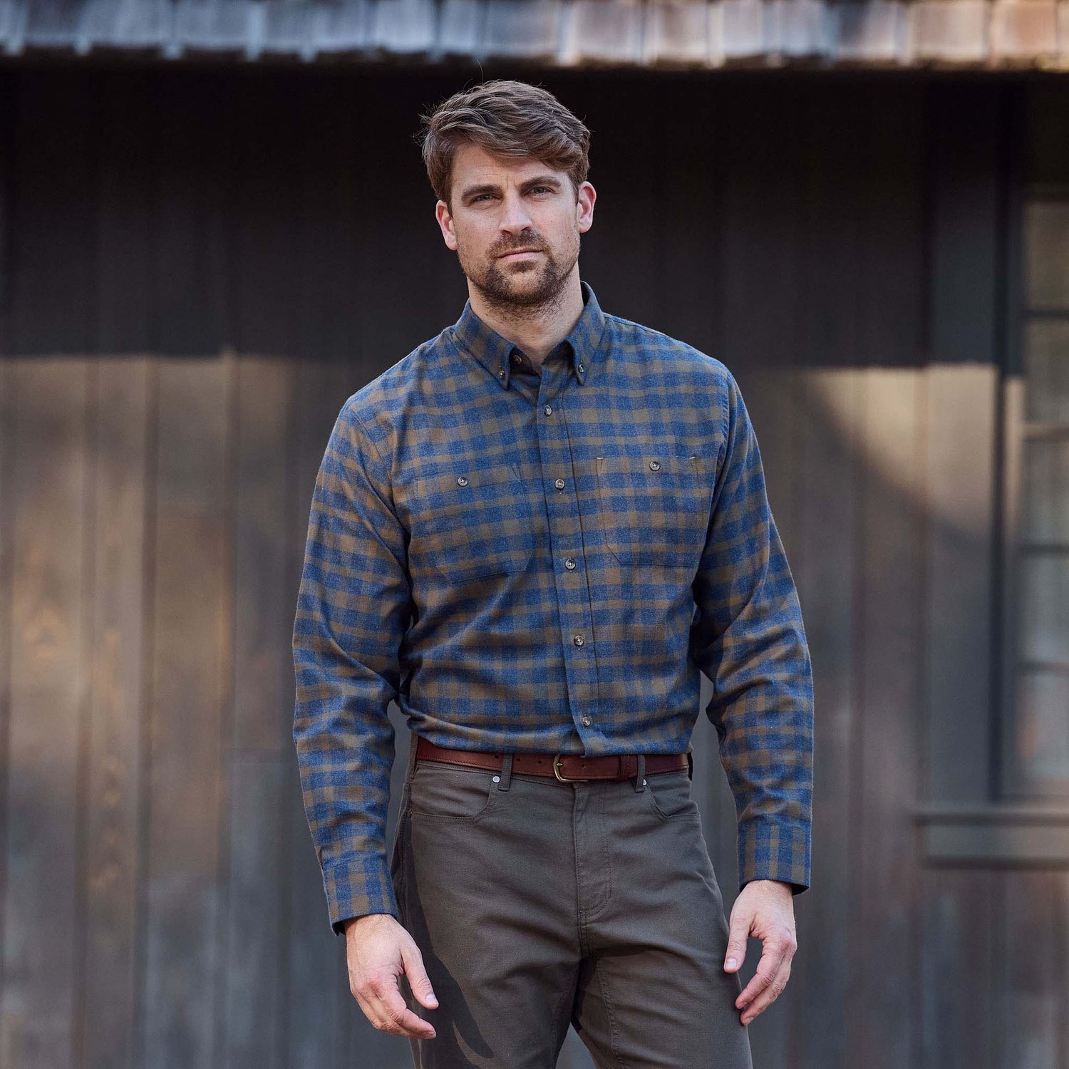 A man stands outside wearing a Tom Beckbe Dixon Brushed Cotton Twill Shirt, tucked into olive pants with a brown belt.