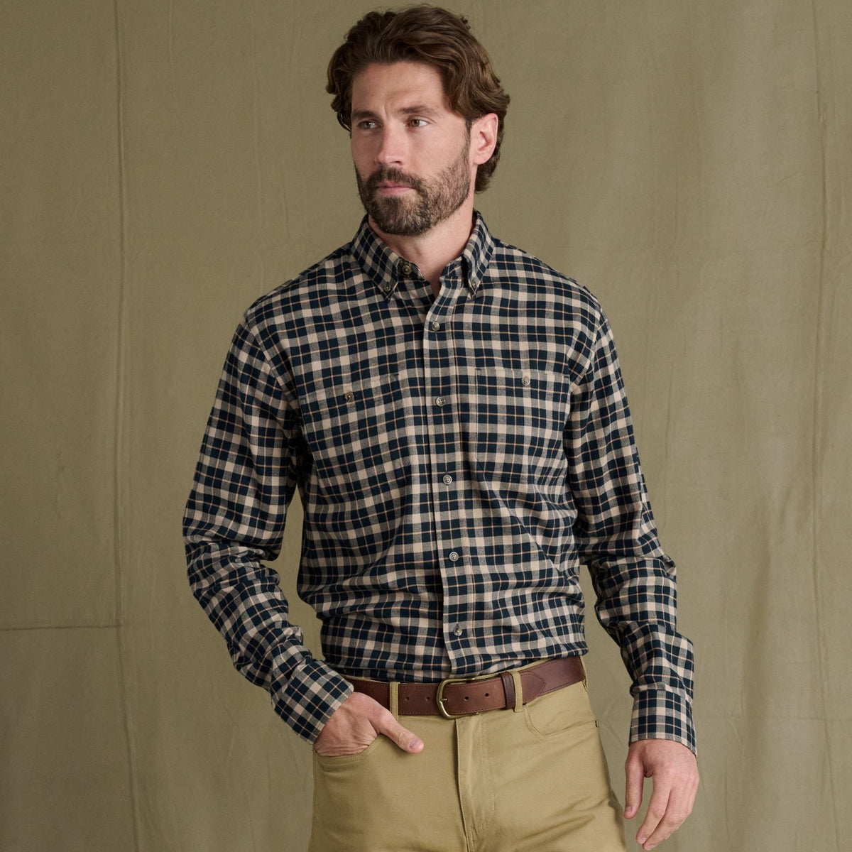 Man in a Tom Beckbe Dixon Brushed Cotton Twill Shirt and khakis stands before a khaki backdrop, hand in pocket.