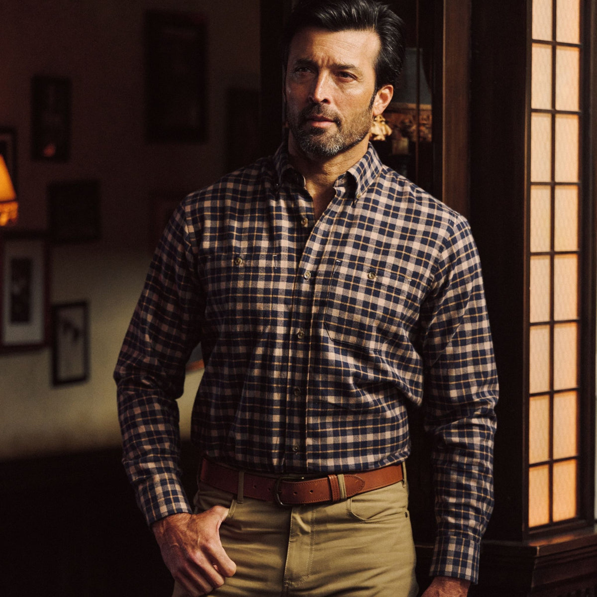 Man in Tom Beckbe Dixon Brushed Cotton Twill Shirt stands by a wooden window under warm, gentle indoor light.